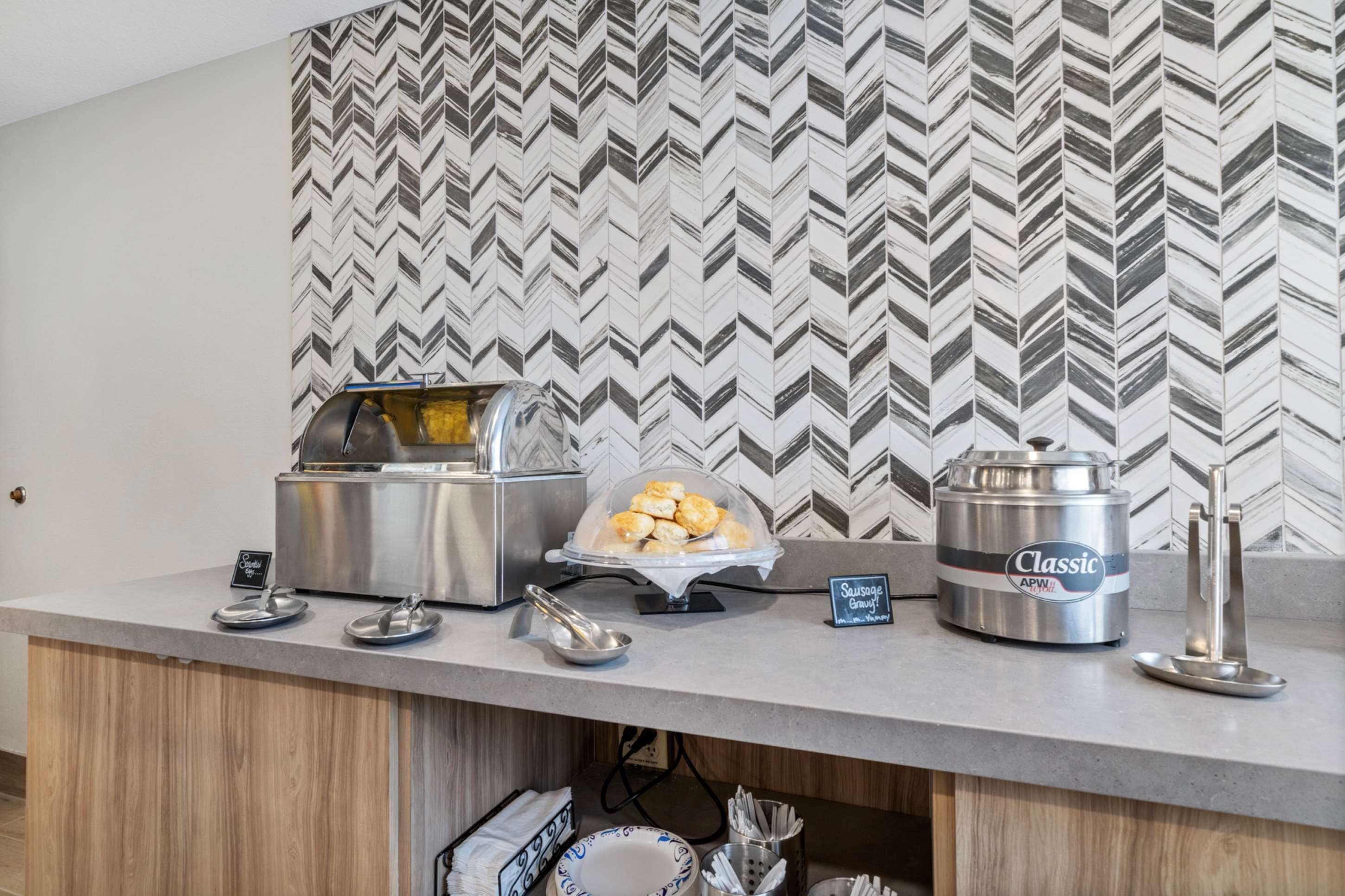 Ein Buffet mit Marmor-Wand, einem Toaster, einer Glasschale mit Gebäck, einer Wurstbehälter und einer Kaffeemaschine.