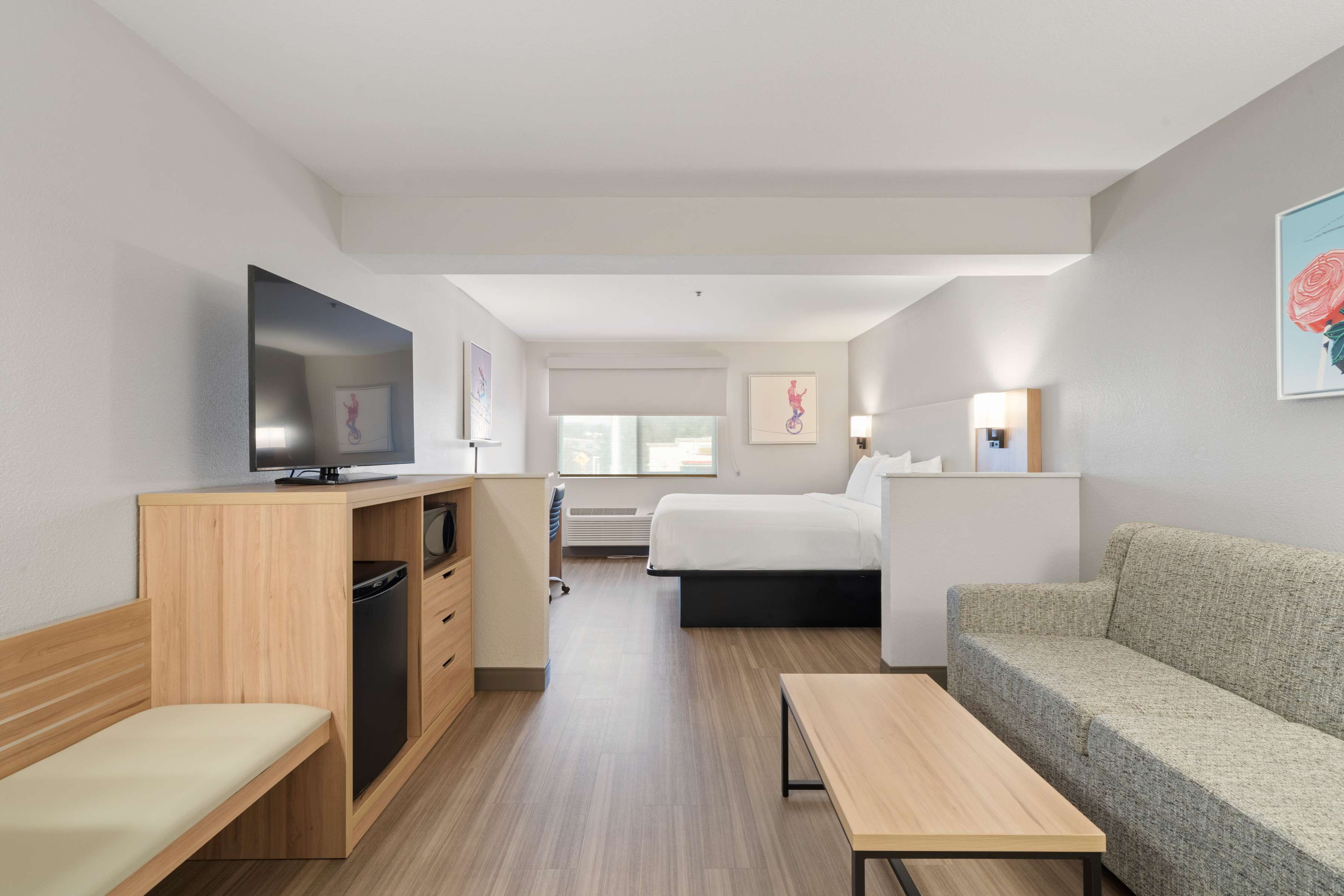 Una habitación de hotel moderna con cama, sofá, televisor, escritorio y una banca.