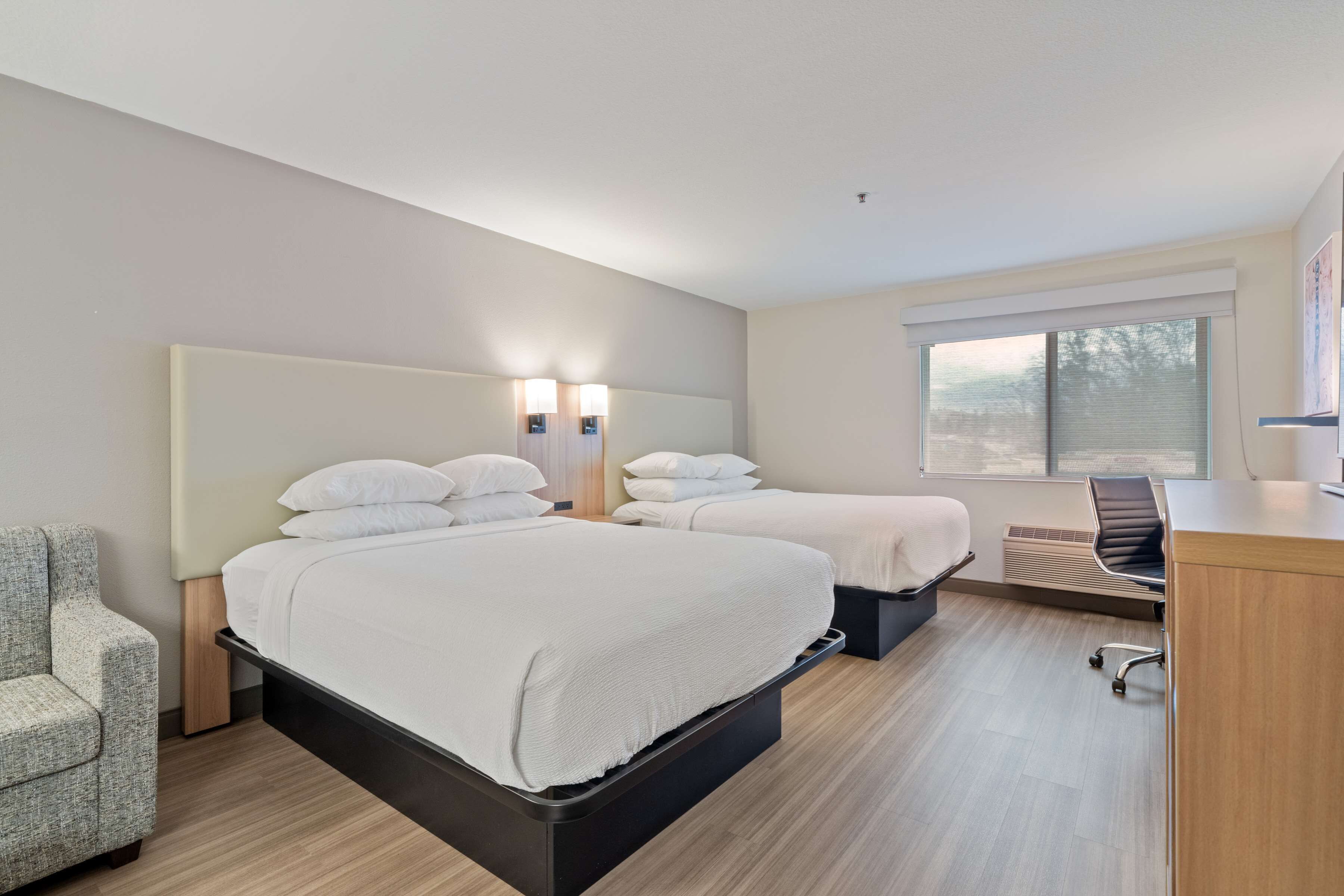 A hotel room with a large bed, two bedside tables, a chair, a desk, and a window with blinds.