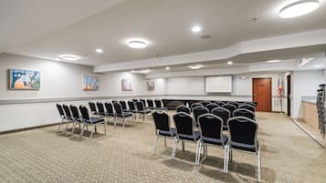Un salón de conferencias con filas de sillas, una pantalla de proyector y obras de arte en las paredes.