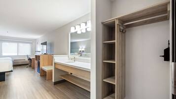 A modern hotel room with a wooden floor, a large mirror, a vanity with a sink, and a built-in wardrobe.