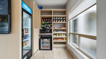 A narrow hallway with a refrigerated beverage dispenser, snack shelves, and a small refrigerator.