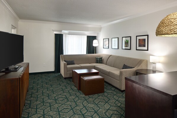 A hotel room with a beige sofa, a wooden coffee table, a TV on a wooden stand, and a patterned carpet. - Ohio University Inn & Conference Center (Athens)