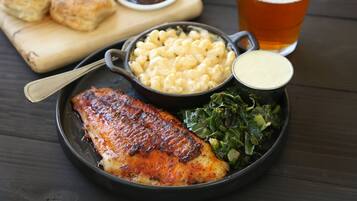 A plate with grilled fish, macaroni, greens, and biscuits, accompanied by a glass of beer.