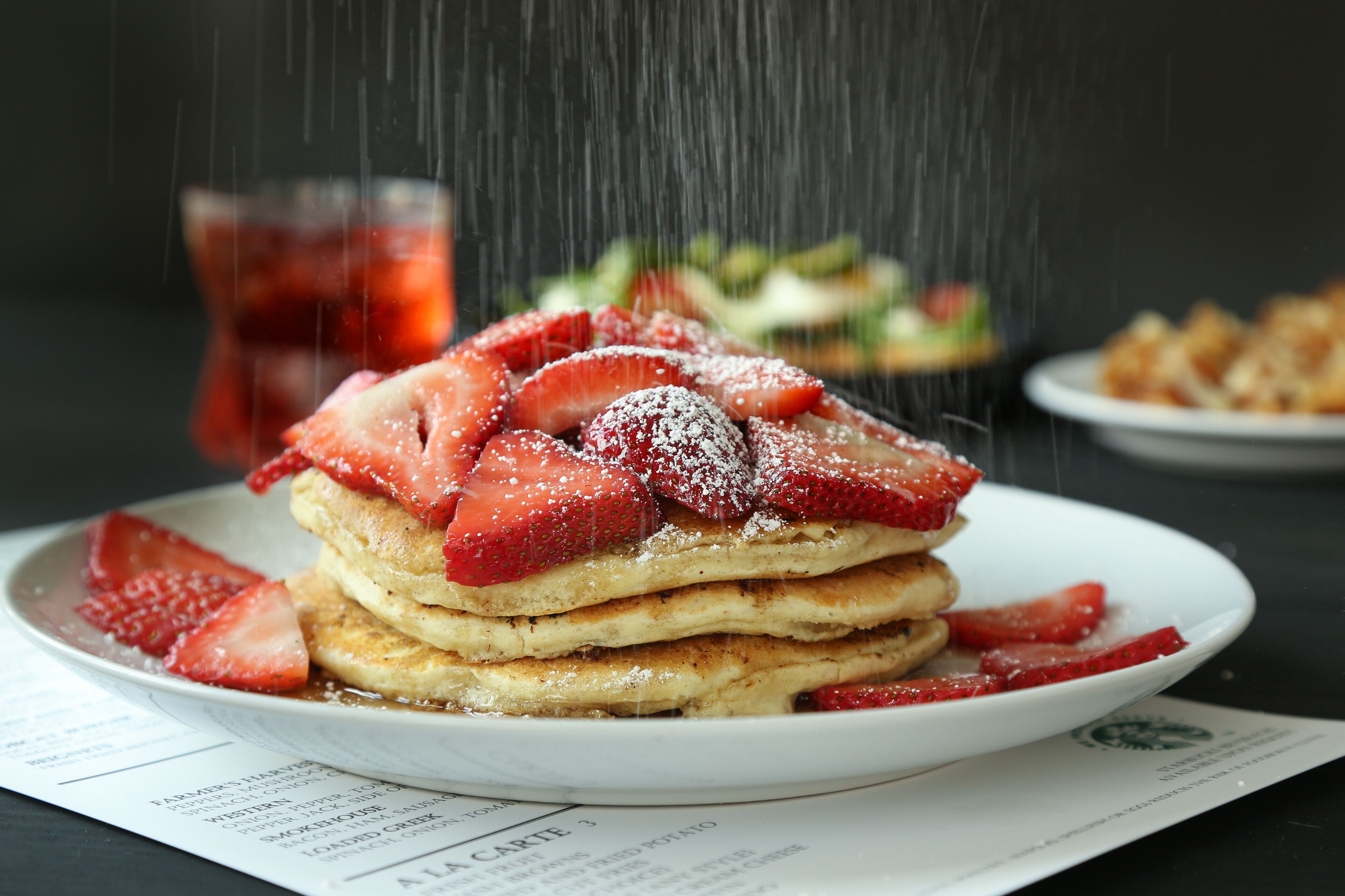 Una pila di pancake con fragole e zucchero a velo su un piatto.
