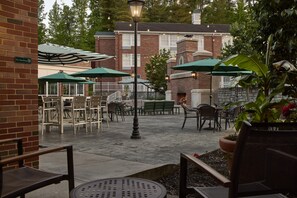 An outdoor patio area with tables and chairs, umbrellas, and a brick building in the background.