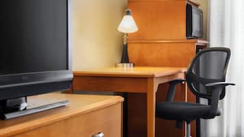 Habitación de hotel con escritorio de madera, televisor, lámpara, silla y minibar.