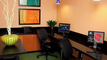 A conference room with a black desk, two black office chairs, a green vase, two framed artworks, a potted plant, and two monitors displaying graphs.