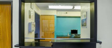 Un área de recepción con un panel de vidrio, una puerta de madera, una pared azul y un escritorio negro con una computadora.