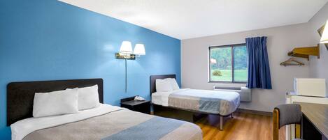 A hotel room with two beds, a desk, a chair, a lamp, and a window with curtains.