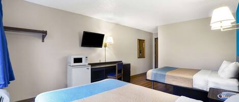 A hotel room with two beds, a desk with a microwave, a TV, and a lamp.