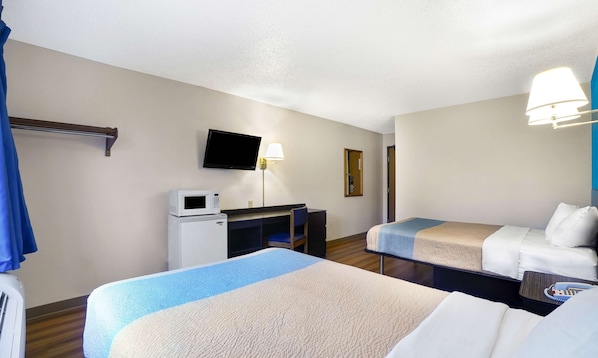 Una habitación de hotel con dos camas, un escritorio con microondas, un televisor y una lámpara.