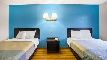 A hotel room with two beds, a nightstand with a phone, and a wall-mounted lamp.