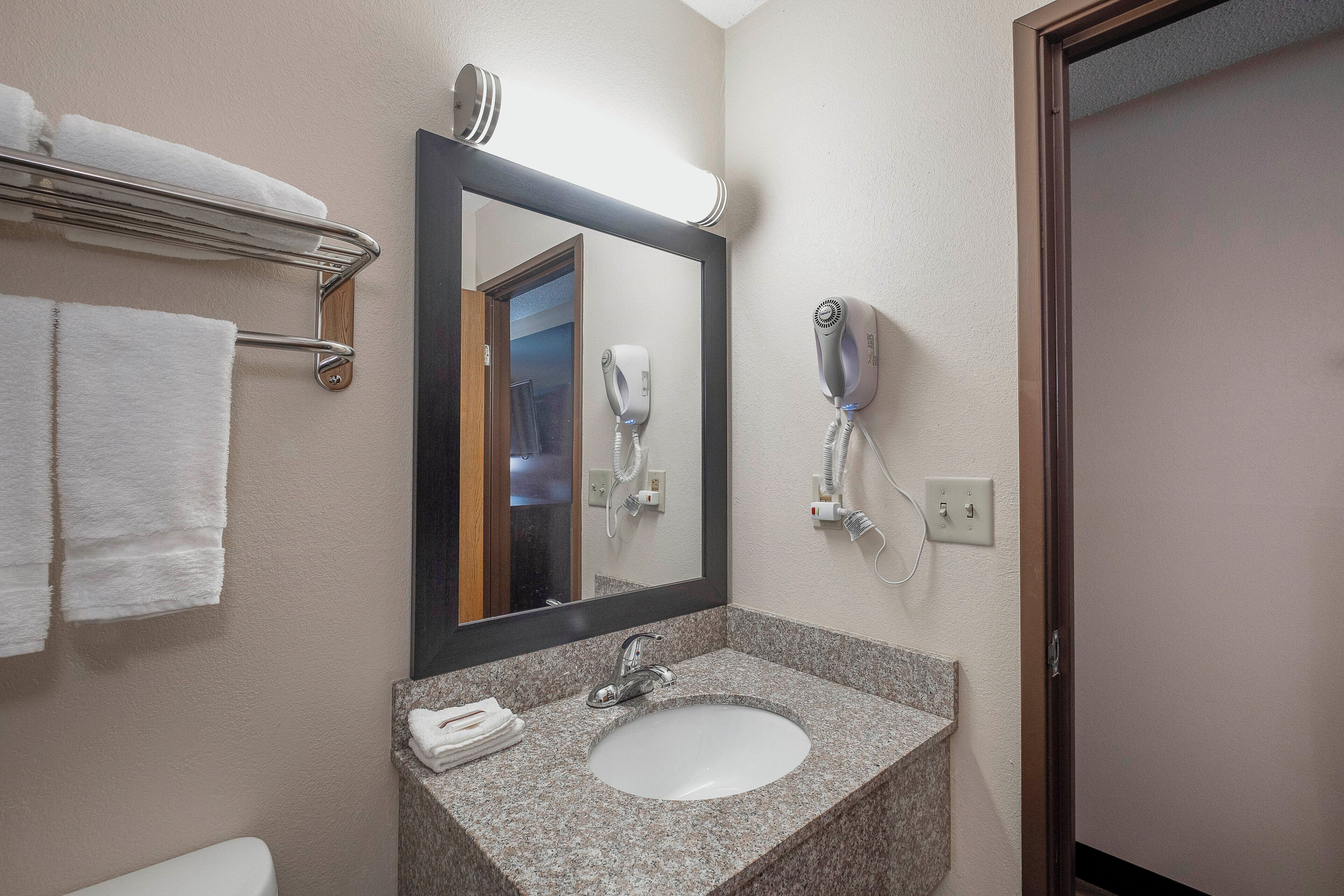 Un baño con lavamanos de granito, un espejo, un perchero para toallas y un secador de pelo.