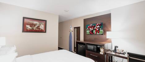 A hotel room with a bed, a desk, a television, and a framed picture on the wall.