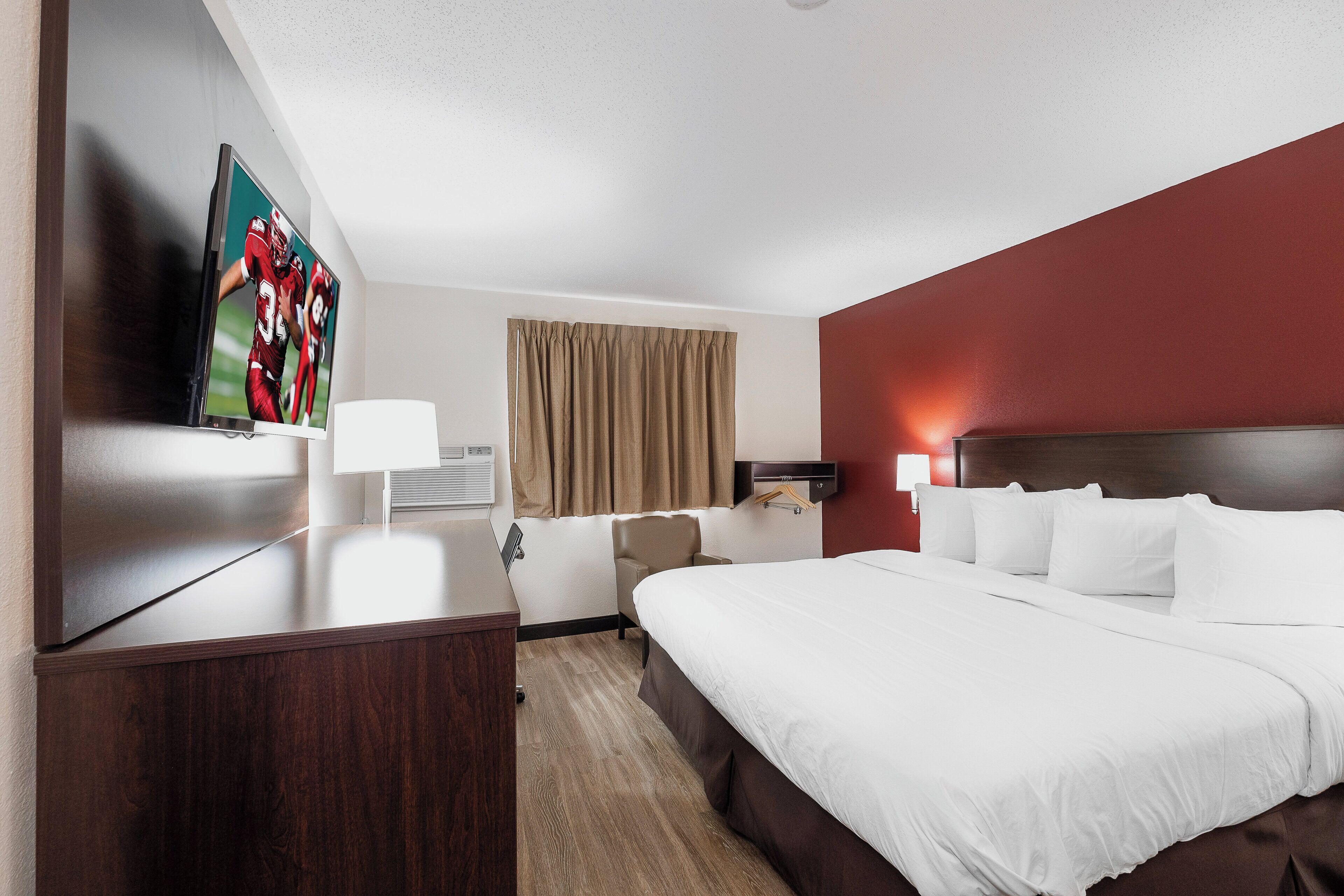 A hotel room with a bed, a desk, a television, and a window with curtains.