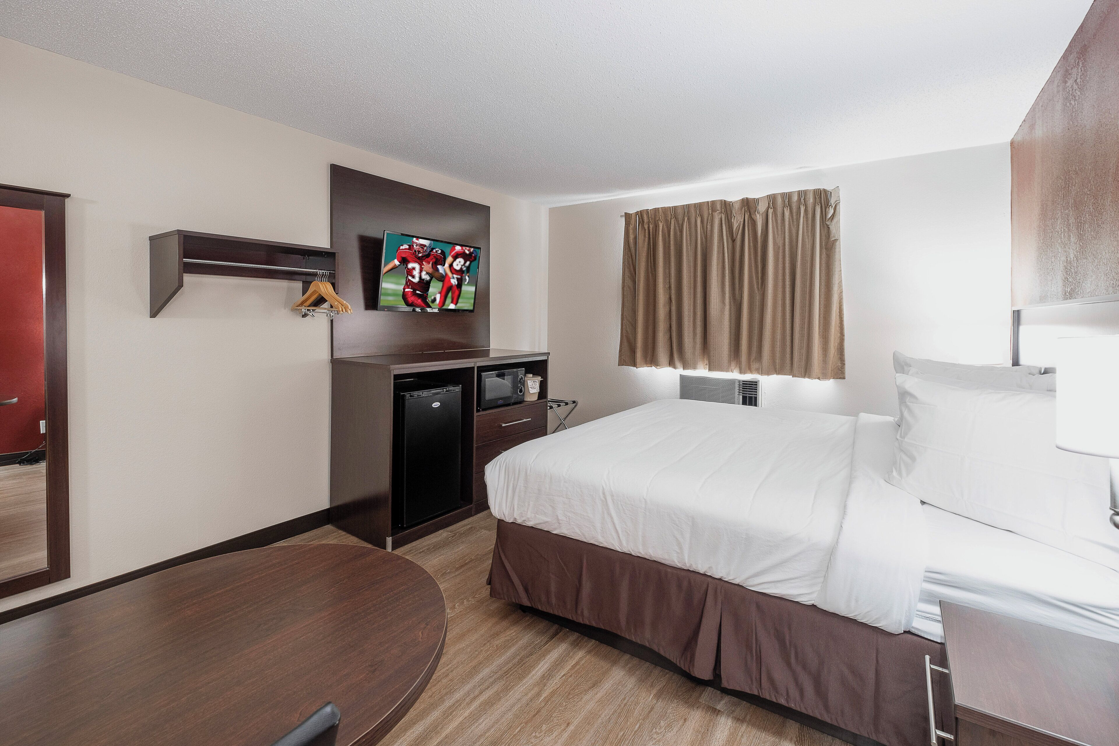 Habitación de hotel con cama, escritorio, televisor y refrigerador pequeño.