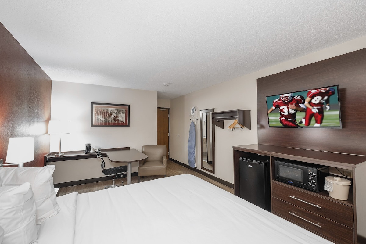 Habitación de hotel con cama, escritorio, silla, microondas, refrigerador y televisión.