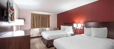 A hotel room with two beds, a desk, a television, and a window with curtains.