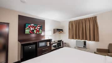 A hotel room with a bed, a desk, a television, a microwave, a heater, and a wardrobe.