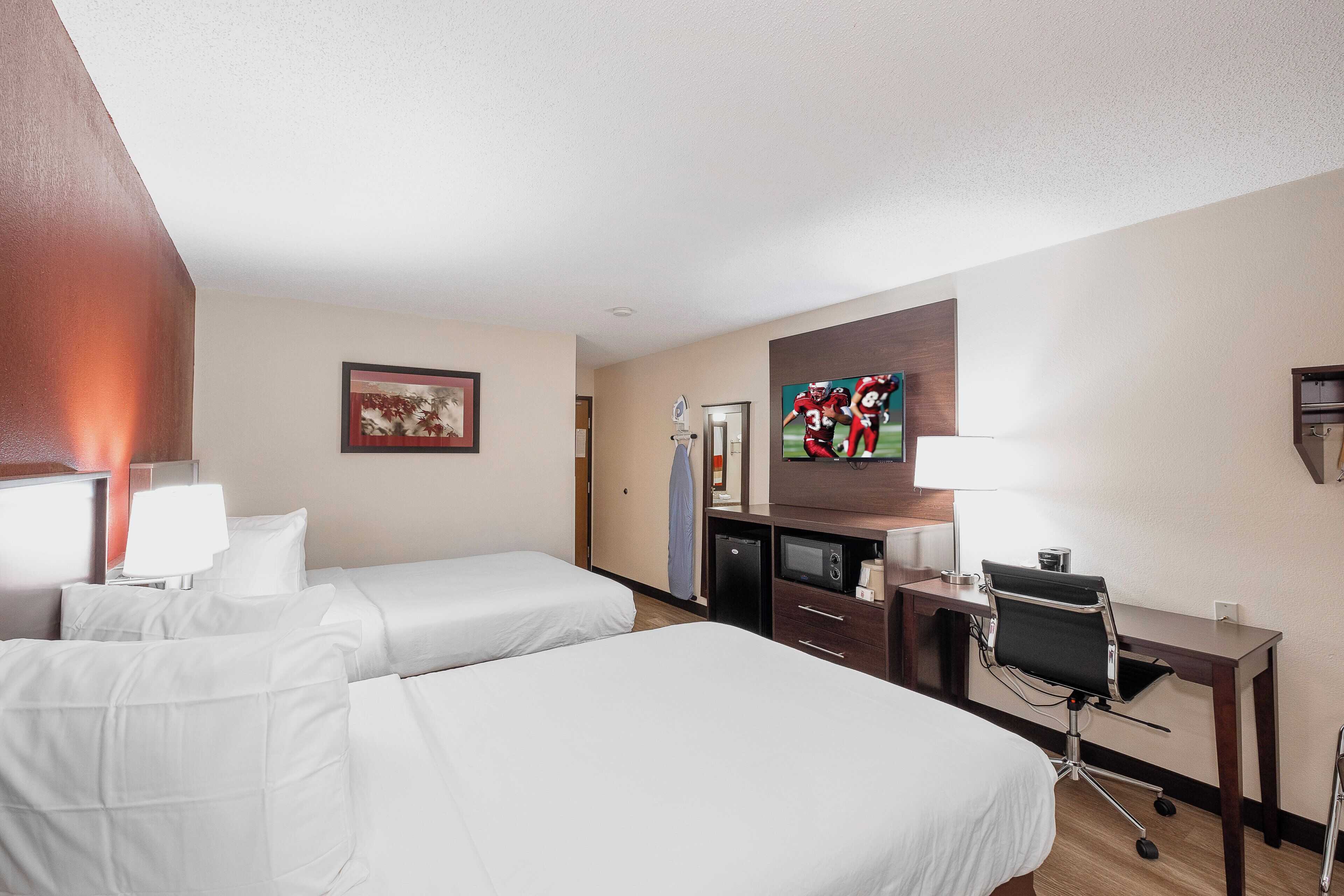 Ein Hotelzimmer mit zwei Einzelbetten, einem Schreibtisch mit Computer, einem Fernseher und einer kleinen Küchenzeile.