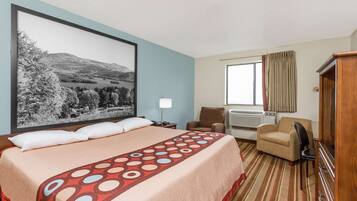 Een hotelkamer met een groot bed, een bureau, een stoel, een dressoir en een groot schilderij aan de muur.