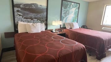A hotel room with two beds, each with a red patterned bedspread, a nightstand with a lamp, and two framed pictures on the wall.