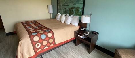 A hotel room with a bed, a nightstand with a lamp, a painting on the wall, and a chair.