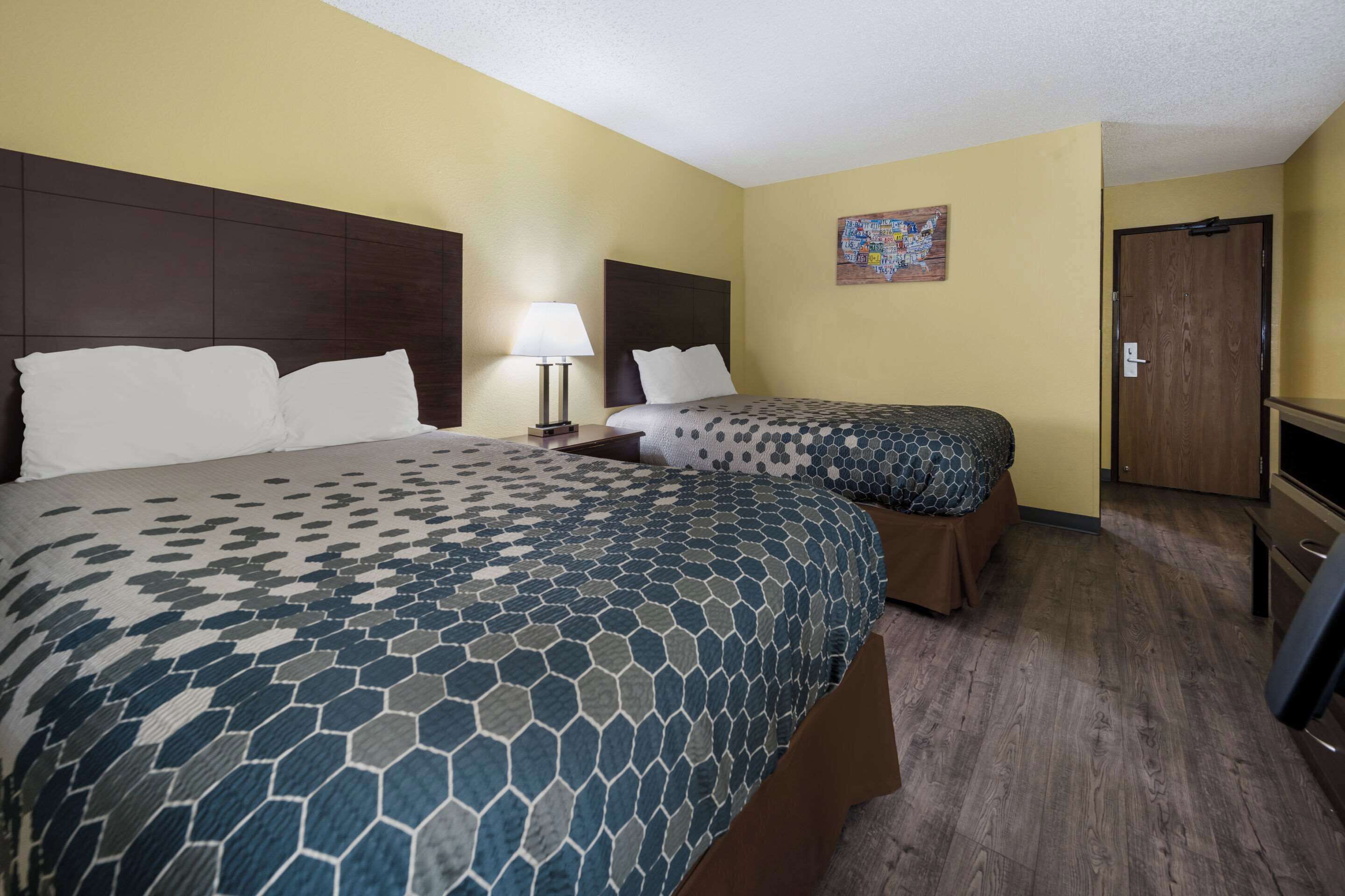 A hotel room with a large bed, a smaller bed, a desk, a chair, a lamp, and a door.