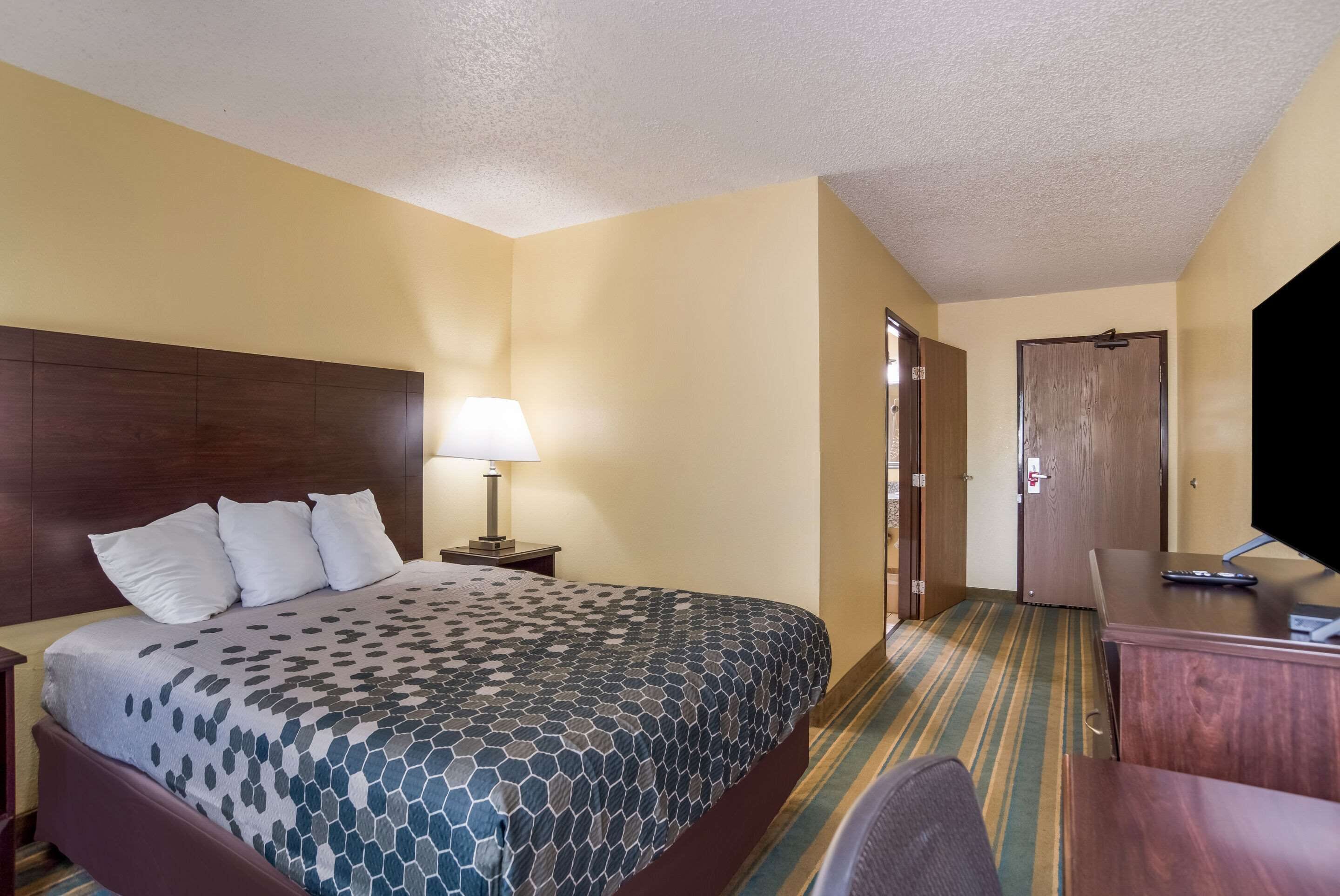 A hotel room with a bed, a desk, a lamp, and a television.