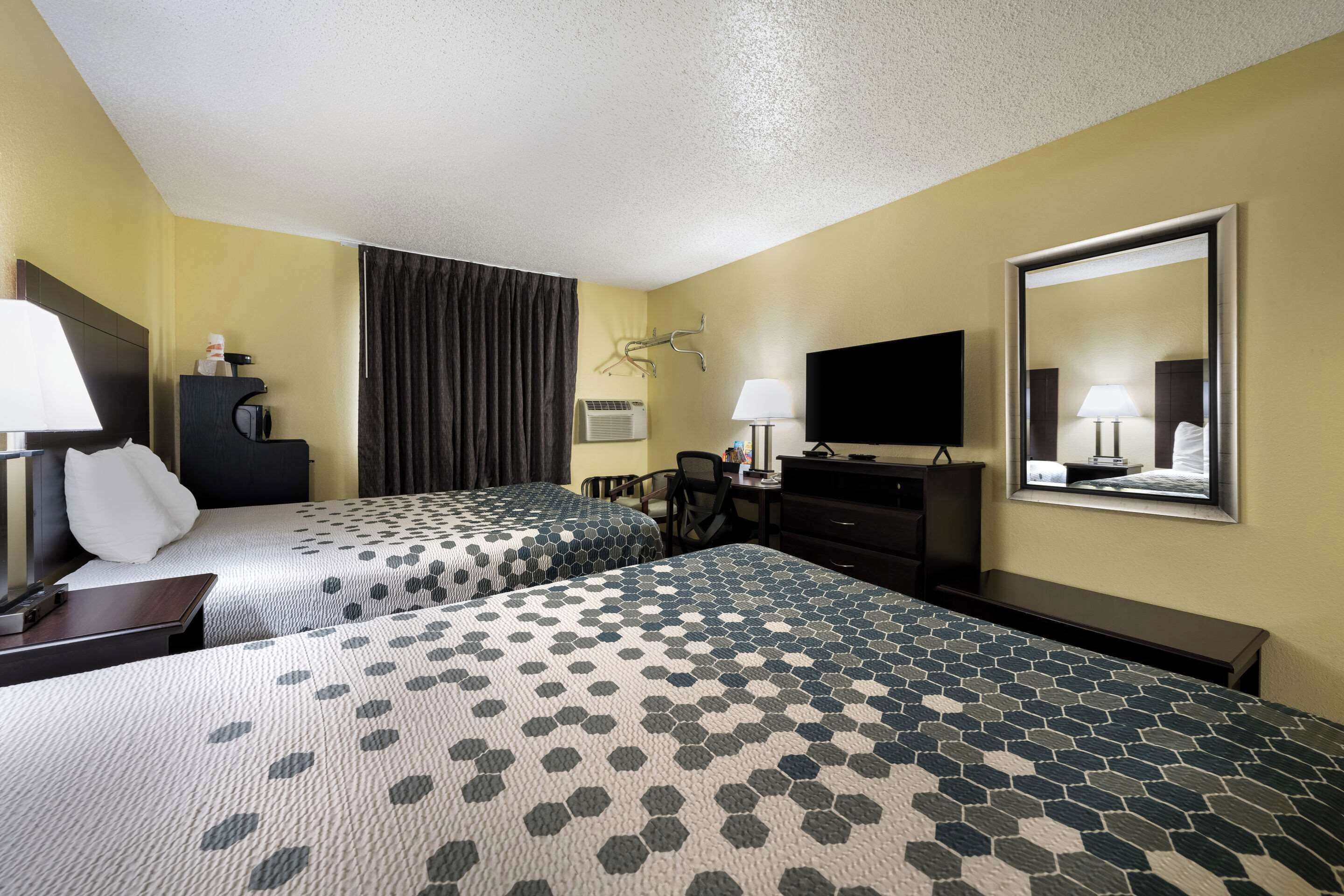 A hotel room with two beds, a desk, a chair, a television, a mirror, and a window with curtains.
