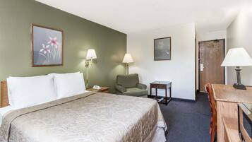 A hotel room with a large bed, a desk, two chairs, a small table, and two wall-mounted lamps.