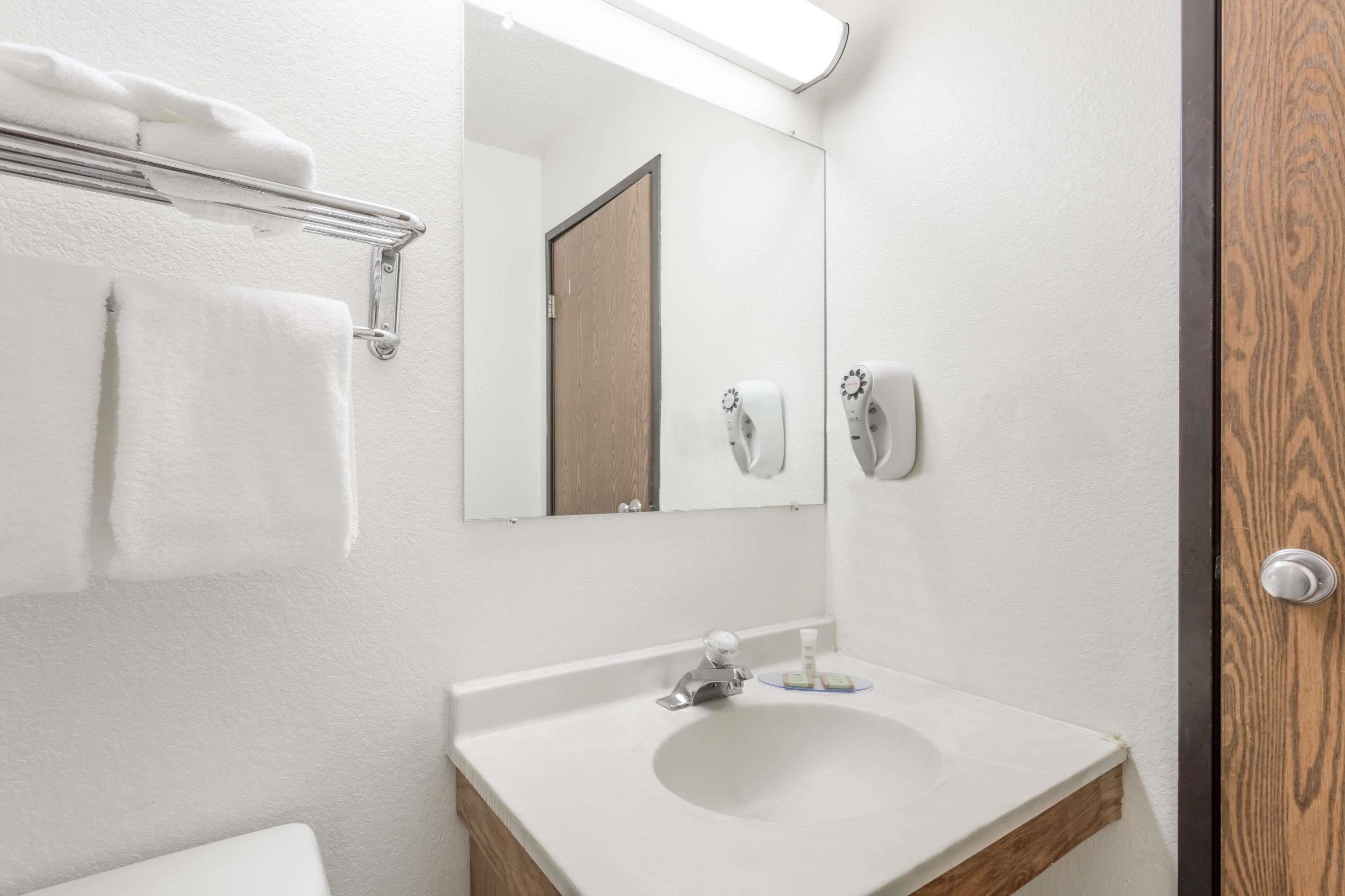 A bathroom with a white sink, a mirror, a towel rack, and a soap dispenser.