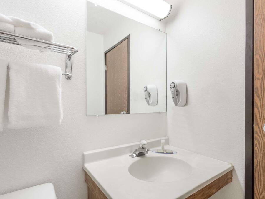 Un bagno con un lavandino bianco, uno specchio, un portasciugamani e un dispenser per sapone.
