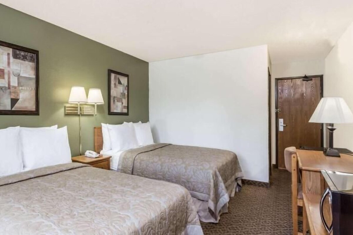Habitación de hotel con dos camas, un escritorio, una silla, dos lámparas de pared y una puerta.