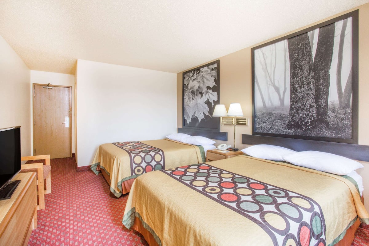 A hotel room with two beds, a TV, a desk, and artwork on the walls.