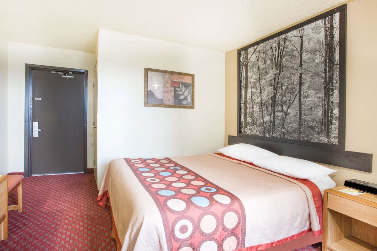 A hotel room with a bed, a painting on the wall, a door, and a carpeted floor.