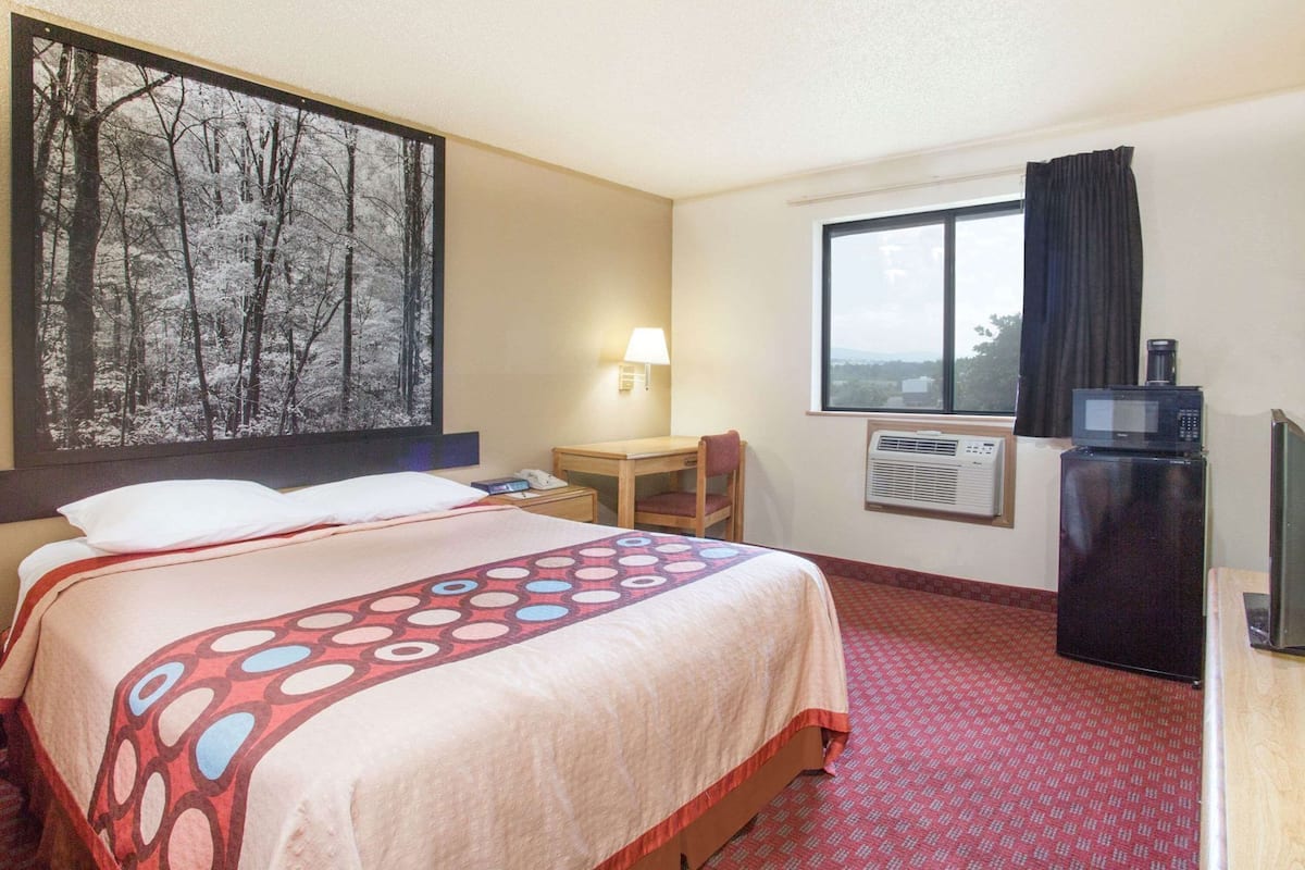 A hotel room with a bed, a desk, a chair, a TV, and a window with a view.