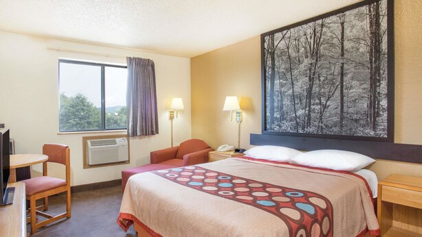 Habitación de hotel con cama, escritorio, silla, ventana con cortinas, aire acondicionado, dos lámparas de noche y un cuadro grande en la pared.