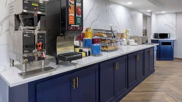 A commercial kitchen with a coffee machine, a juice dispenser, and a pastry display.