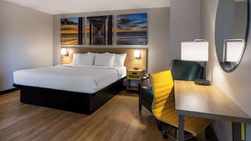 A hotel room with a bed, a desk, a chair, and artwork on the wall.