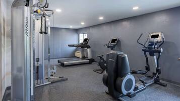 Un gimnasio con máquinas de cardio, una banca para pesas y un espejo.