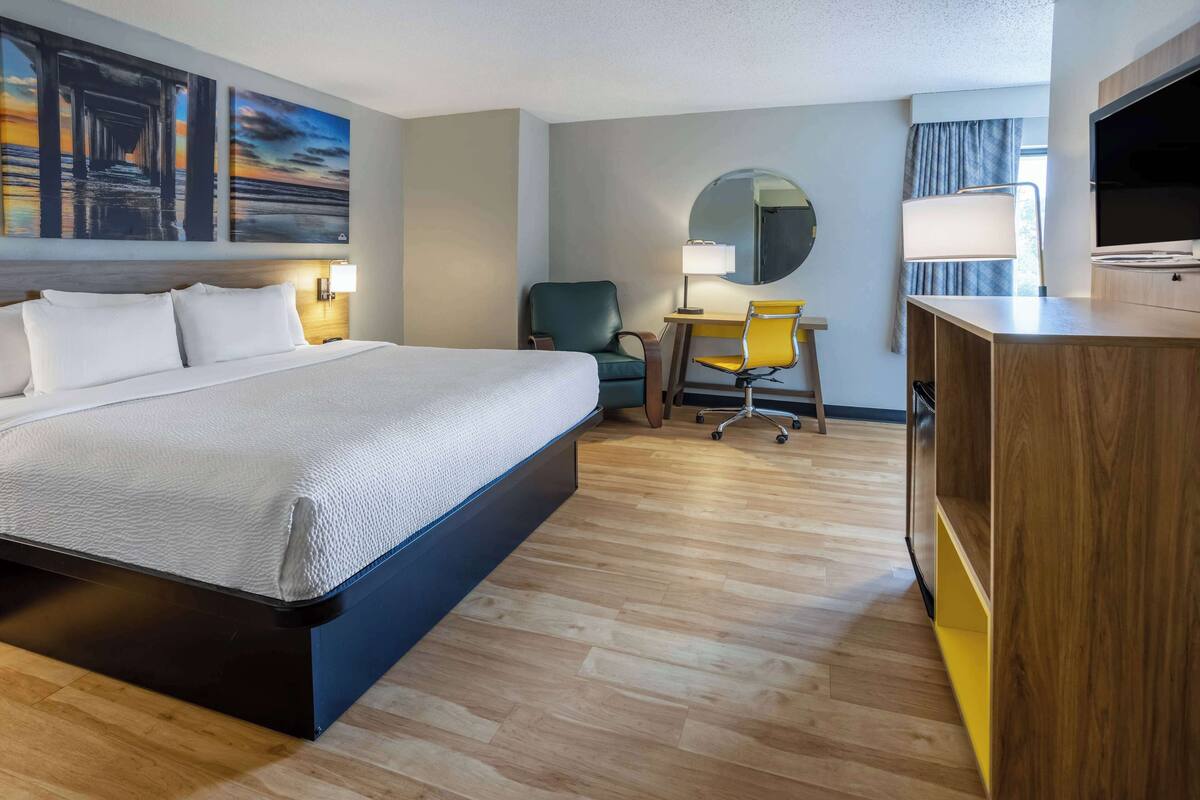 Une chambre d’hôtel avec un grand lit, un bureau avec une chaise, une télévision et des œuvres d’art accrochées au mur.