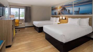 A hotel room with two beds, a desk, a chair, and large windows.