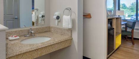 A hotel bathroom with a granite countertop sink, a towel rack with a white towel, a hairdryer, and a mirror.