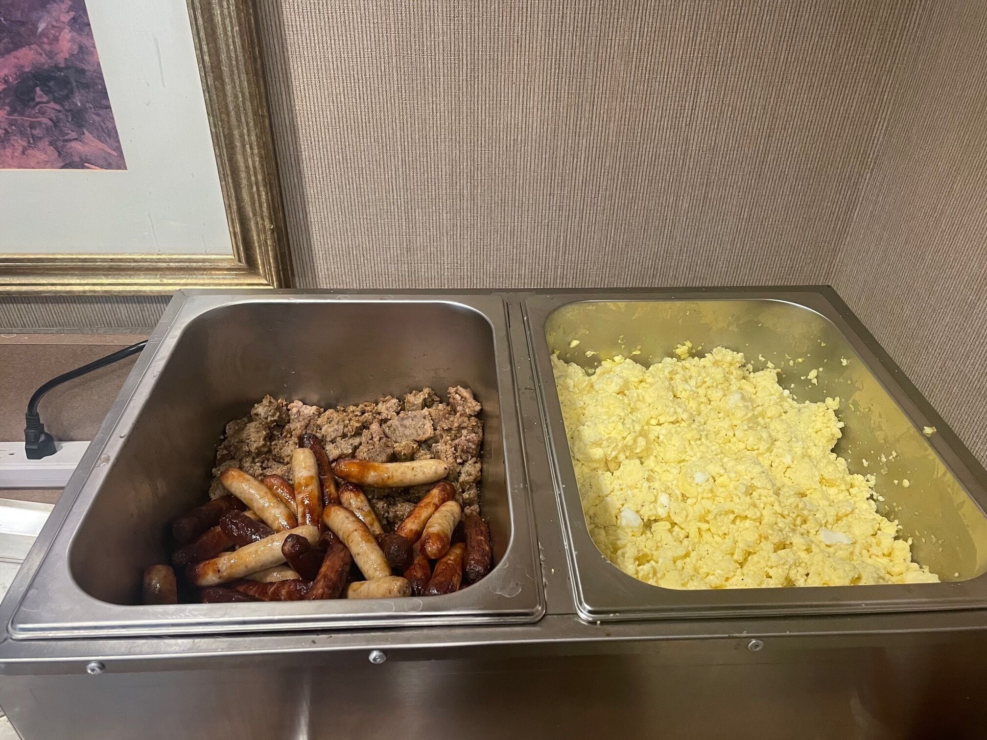 A buffet with two trays: one with cooked sausages and ground meat, and another with scrambled eggs.