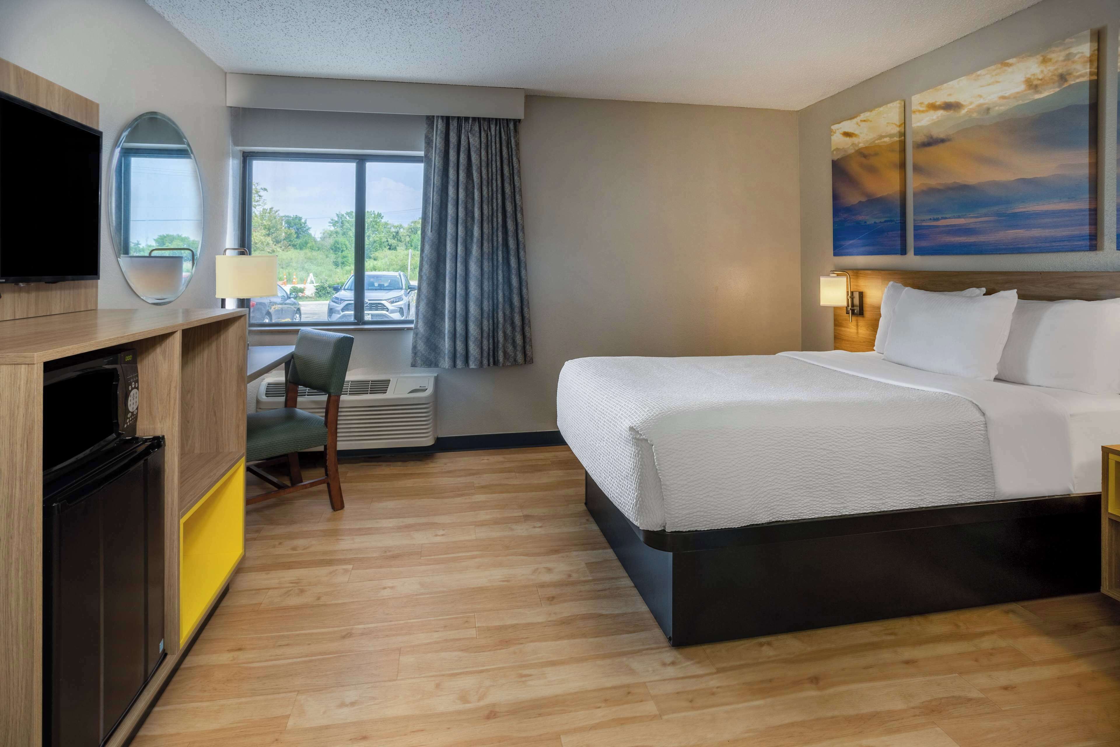 A hotel room with a bed, a desk with a chair, a television, and a window with curtains.