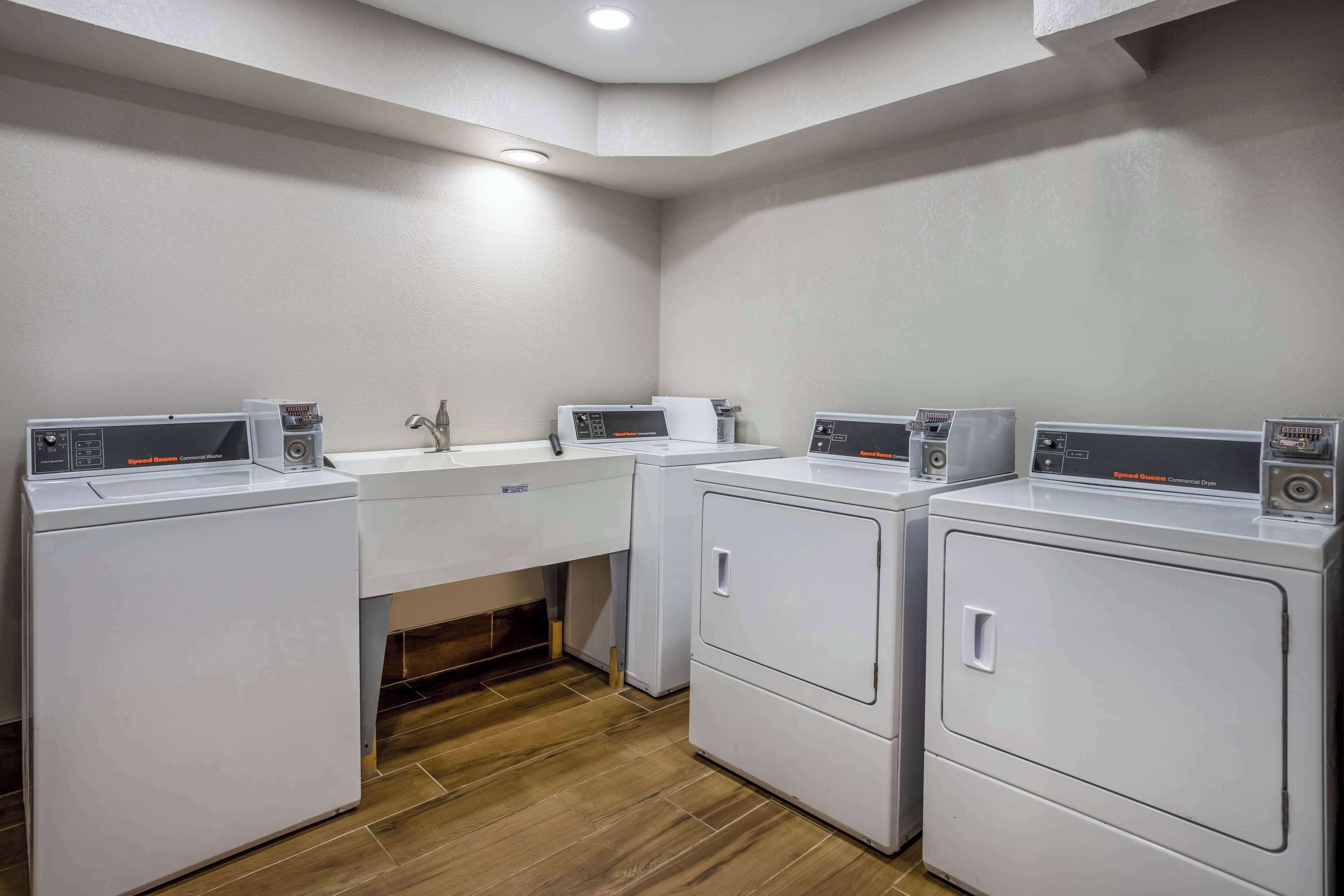 A laundry room with four washing machines and a sink.