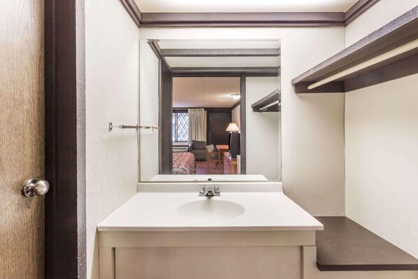 A bathroom with a white sink, a mirror, and a door leading to a bedroom.