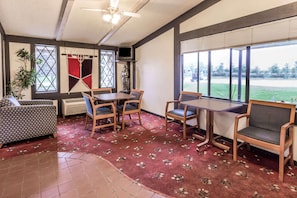 Une pièce comprenant une table à manger, des chaises, un canapé, un téléviseur et une grande fenêtre avec des stores.